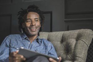A man sits on a sofa, holding a tablet in his hand.