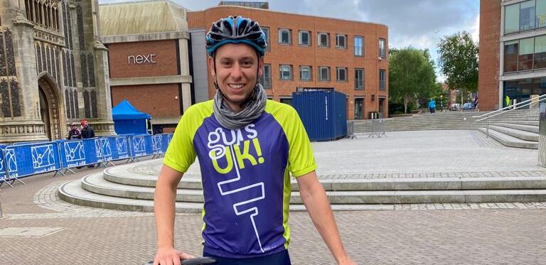James in his Guts UK cycling vest standing behind of his bike, smiling