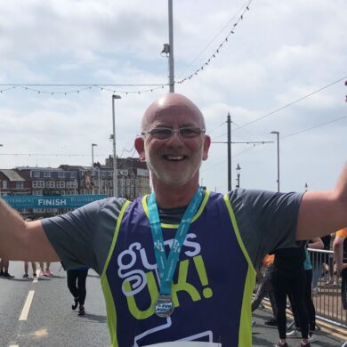 Garry looking happy with his hands in the air after completing a 10k run in his Guts UK running vest