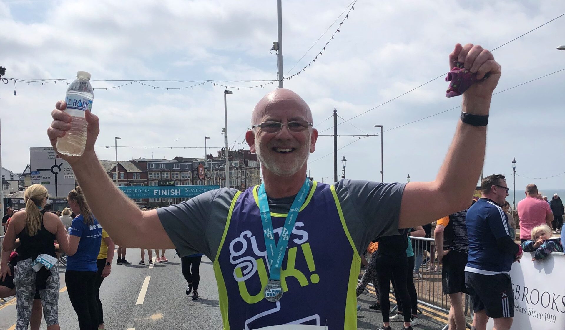 Garry looking happy with his hands in the air after completing a 10k run in his Guts UK running vest