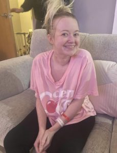 Ellie smiling on the couch with her hair up and in a pink top and black leggings