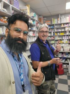 Vishal, at work, and friend smiling at the camera both showing the camera a thumbs up