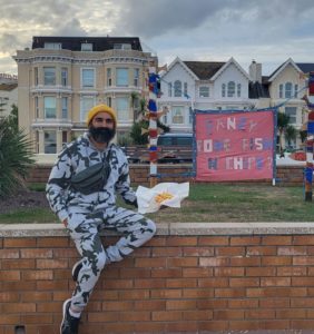 Vishal sat on a wall, fish and chips in his hand. Sign reads "Fancy some fish 'n' chips"