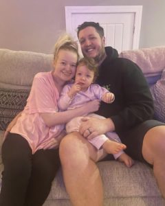 Steph, her husband Alex and 2 year old daughter Ellie cuddling on the couch