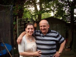 Derek in a stripey top smiling for the camera with one of his daughters