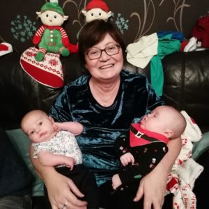 Anne at Christmas time. Holding 2 of her baby grandchildren in her arms, smiling for the camera