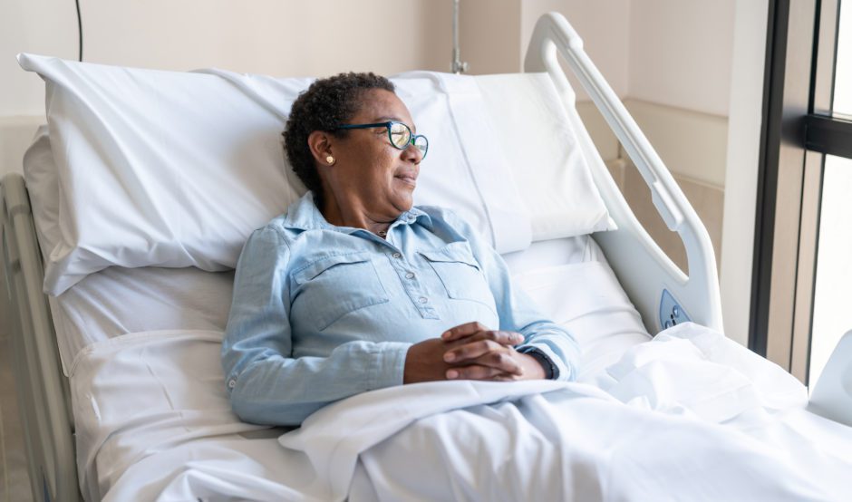 Black adult patient lying down on bed hospitalized looking away to the window very pensive