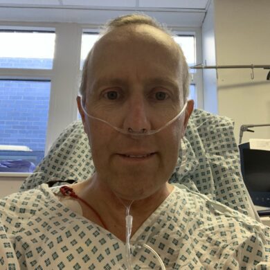 Steven is smiling at the camera in a hospital gown. He has a nasal cannula delivering oxygen.