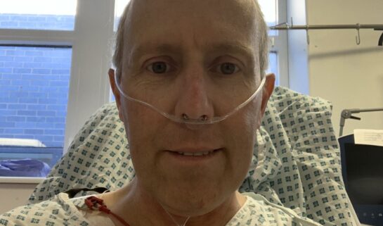 Steven is smiling at the camera in a hospital gown. He has a nasal cannula delivering oxygen.