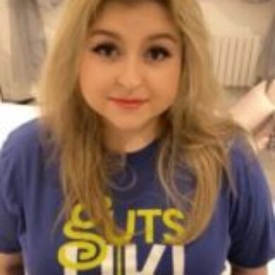 Becca is wearing a Guts UK t-shirt and smiling at the camera.