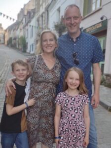 Sarah's family with her husband, son and daughter. Her husband is stood next to her and their children are in front. They are on the streets in a European city and all smiling at the camera.