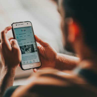 This is seen behind the back of a man's head while he is holding his phone with both hands and staring at the screen reading the information present.