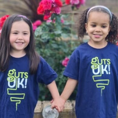 Grace and Alia are smiling at the camera in their Guts UK t shirts and holding hands.
