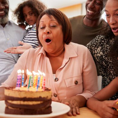 A woman blows out the candles on her birthday cake as she is surrounded by her family.