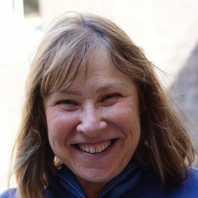 Dani has short, light coloured hair and is wearing a blue t-shirt. She is smiling at the camera.