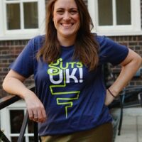 Katie is smiling at the camera and wearing a Guts UK t-shirt.