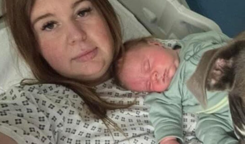 Amee is propped up in a hospital bed wearing a hospital gown, holding her baby and her assistance dog, a grey Staffy, is also in the photo
