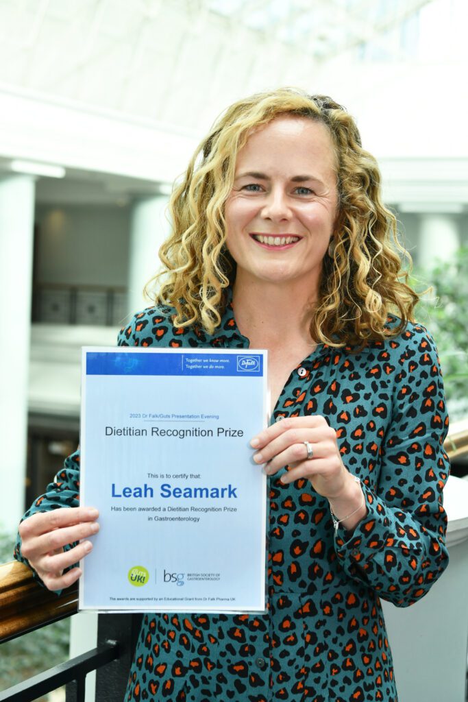 Leah is holding her certificate and smiling at the camera.