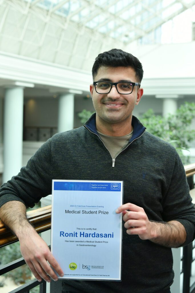 Ronit holds his awards certificate and is smiling at the camera