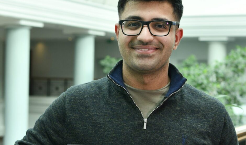 Ronit is holding his awards certificate and smiles at the camera