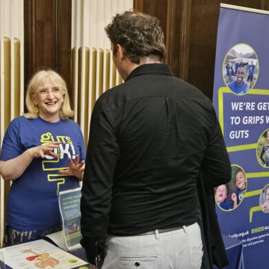 A member of Guts UK's staff team is standing behind a table with information leaflets. They are talking to a person on the other side of the table, who has their back to the camera.