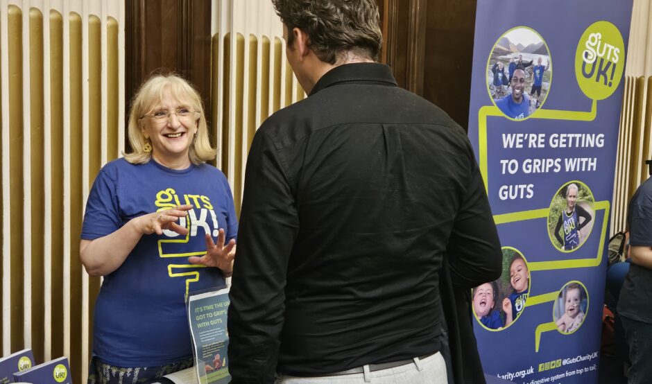 A member of Guts UK's staff team is standing behind a table with information leaflets. They are talking to a person on the other side of the table, who has their back to the camera.