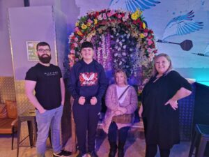 Cornelius's family members including two males and two females are happily looking at the camera. They are indoors and there is a flower archway behind them.