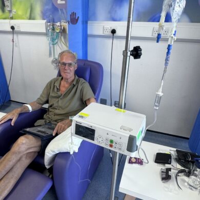 Graham is sat in a blue hospital chair, receiving chemotherapy treatment via a line into his arm.