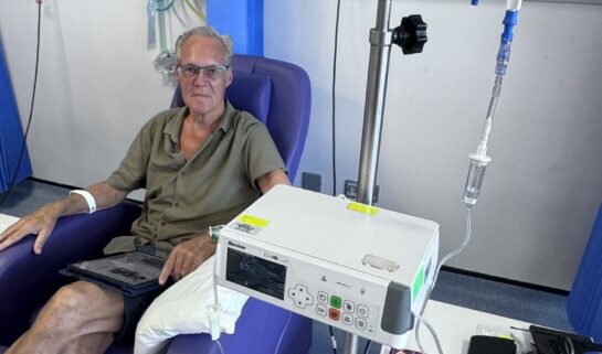 Graham is sat in a blue hospital chair, receiving chemotherapy treatment via a line into his arm.