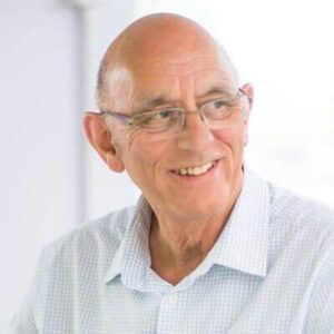 Dave is wearing glasses and a white shirt. He is smiling towards his left. Only his head and shoulders are seen in the image. 