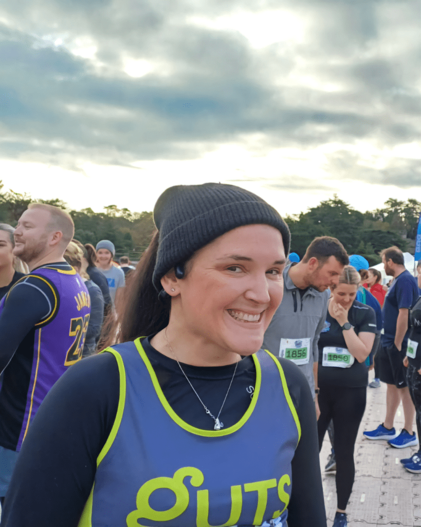Rachel is smiling at the camera, wearing a Guts UK running vest, with a long sleeve black top underneath.