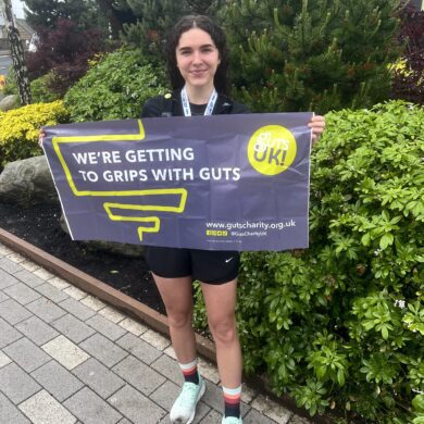 Briony is holding a Guts UK banner and is standing after running the Edinburgh Half Marathon.
