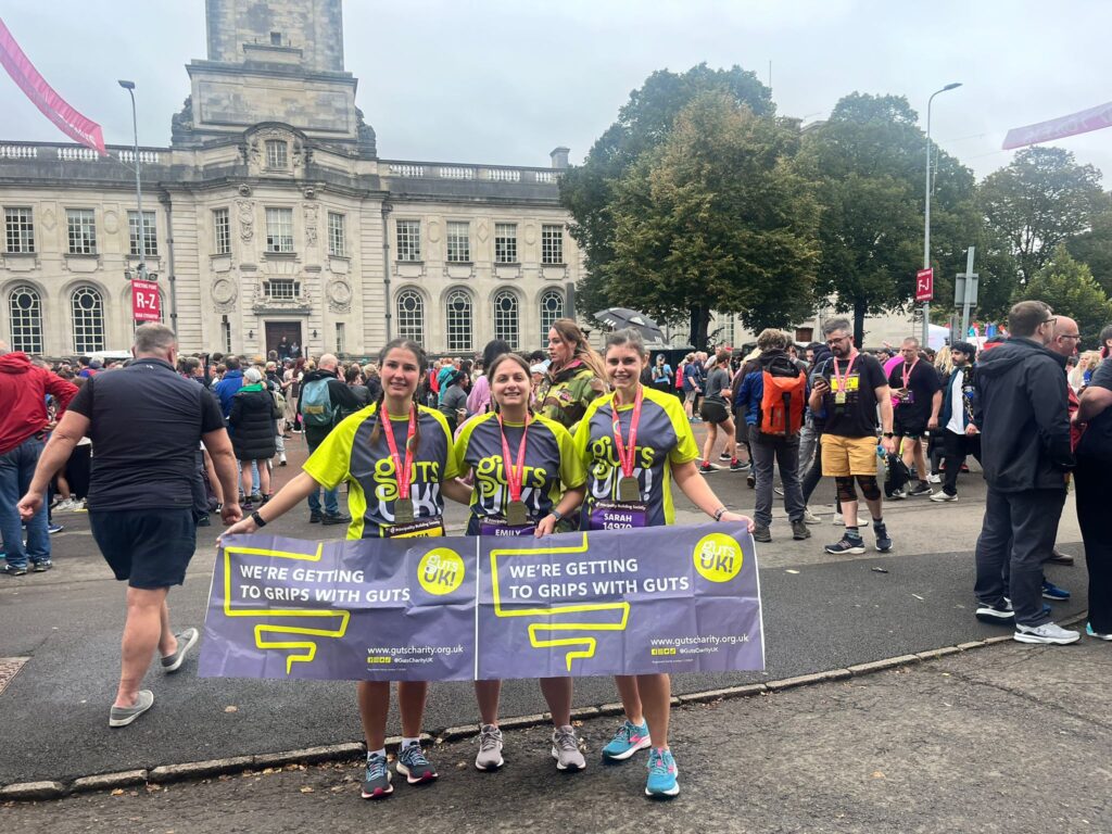 Emily and Guts UK supporters stand with their running medals with a Guts UK banner