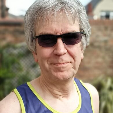 Steve is smiling at the camera. He is wearing sunglasses and a Guts UK running vest.