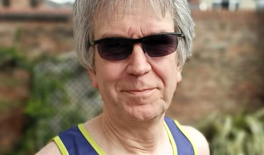 Steve is smiling at the camera. He is wearing sunglasses and a Guts UK running vest.