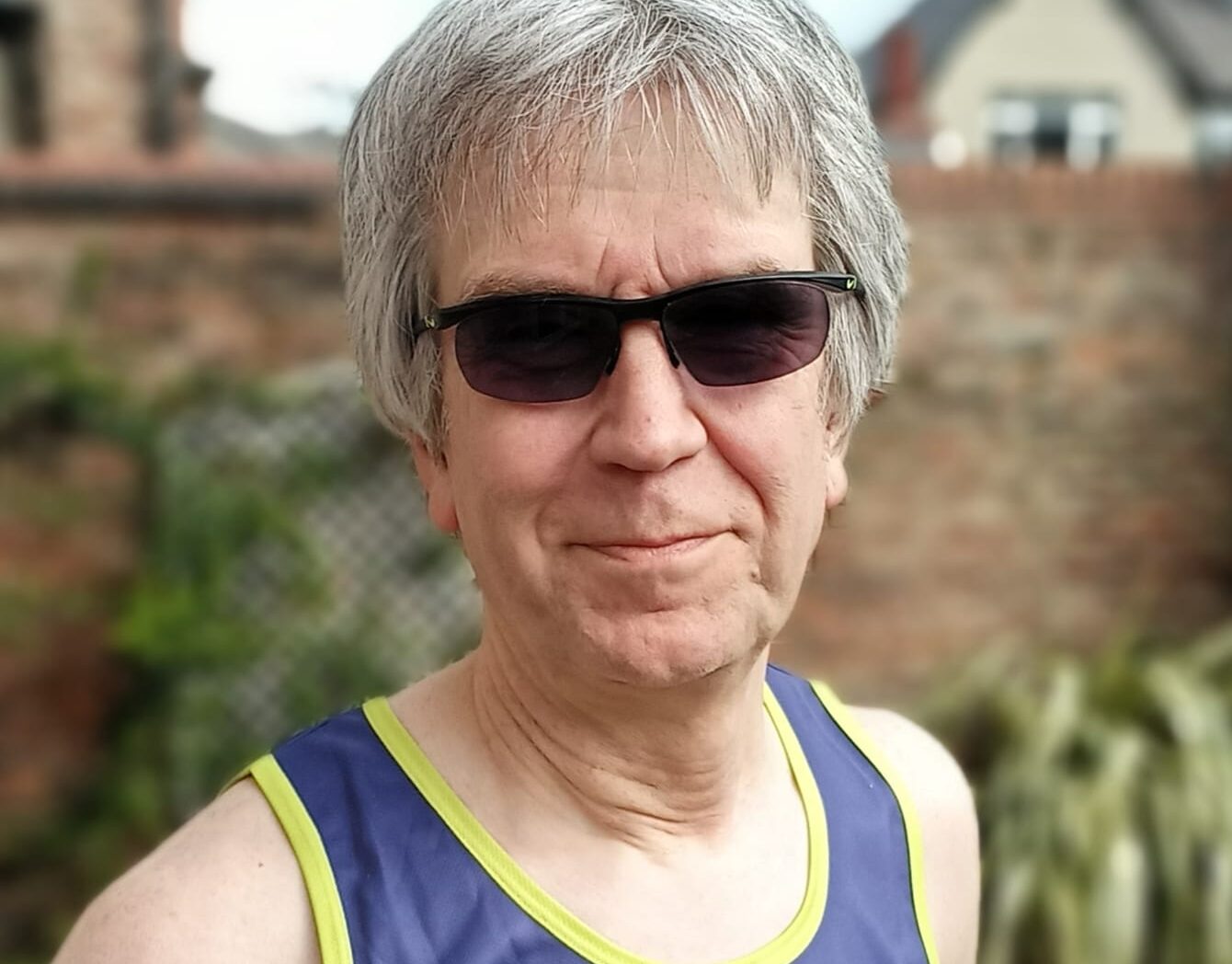 Steve is smiling at the camera. He is wearing sunglasses and a Guts UK running vest.