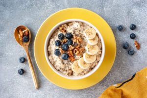 A yellow bowl with porridge, blueberries, banana and nuts.