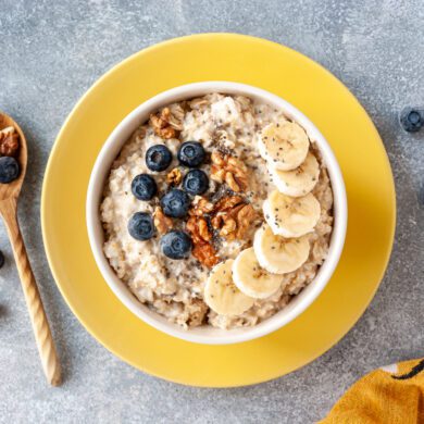 A yellow bowl with porridge, blueberries, banana and nuts.