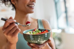 A person eating fruit and yogurt out of a bowl.