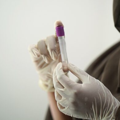 A person wearing gloves is holding a blood collection tube.