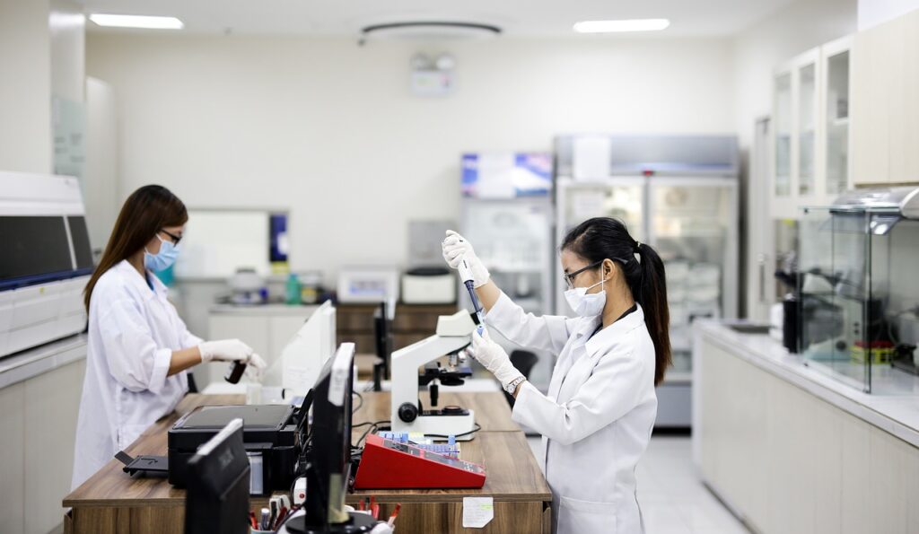 Two female scientists are in a lab. One of them is holding a tube and a pipette.
