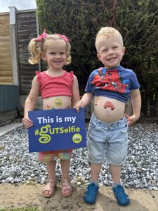 Imogen and her brother are in the garden taking part in the #GUTSelfie campaign. They’re both smiling at the camera with #GUTSelfie temporary tattoos on their bellies. Imogen is also holding the #GUTSelfie board in front of her.