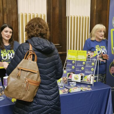 Two of our team members are stood behind an information stand, with Guts UK leaflets and posts. They are talking to two people of the other side of the table.