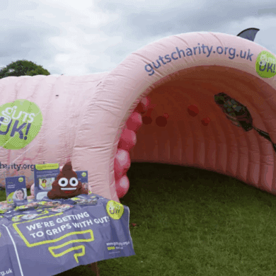 A pink, giant inflatable colon, named Colin, next to a Guts UK information stand.