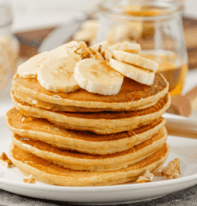 A stack of pancakes on a plate, topped with sliced banana.
