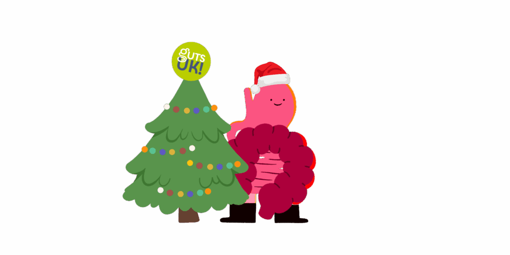 Guts UK's brand character cartoon of the gut organ wears a red and white Santa hat and is stood next to a green Christmas tree, smiling. The tree has string lights on it of various colours and a Guts UK logo as the star on the top of the tree.
