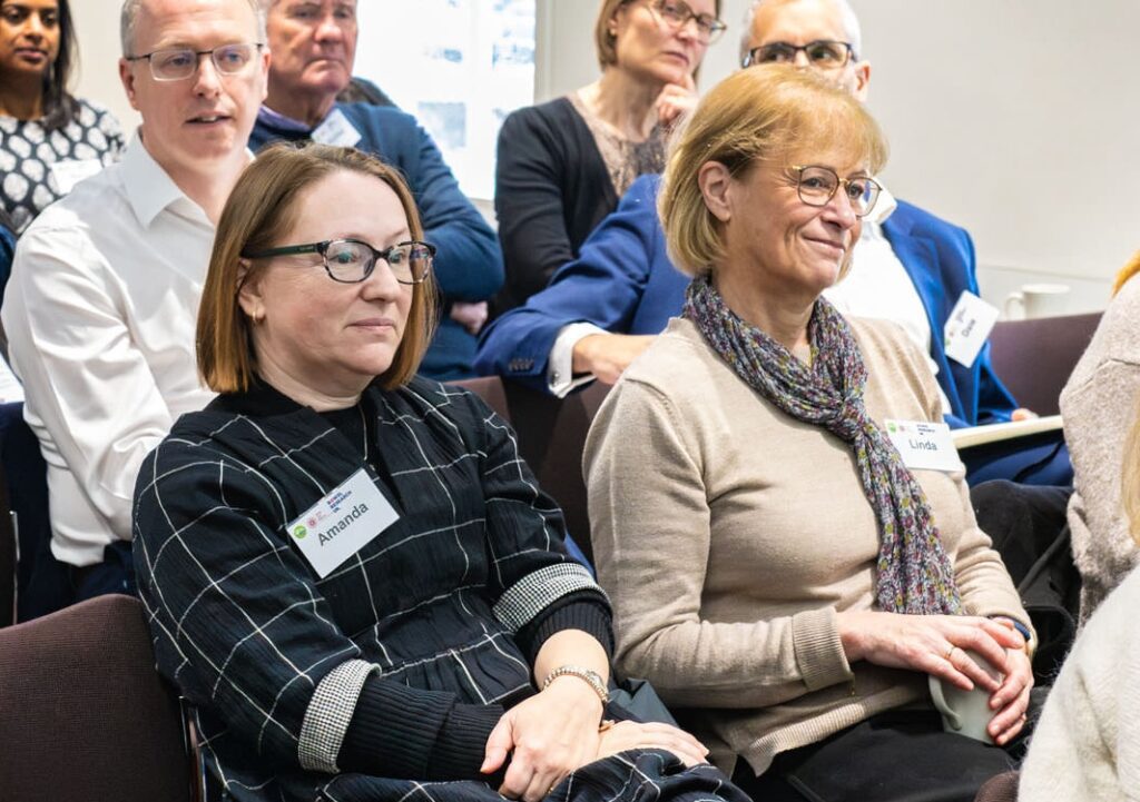 Two patients sit together in an audience, listening to someone speak.