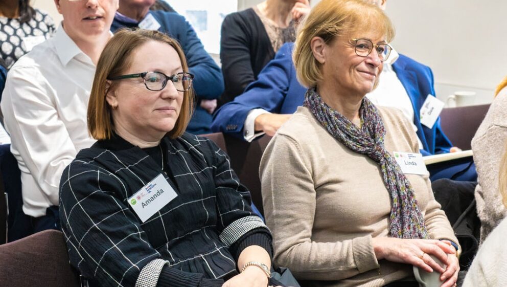 Two patients sit together in an audience, listening to someone speak.