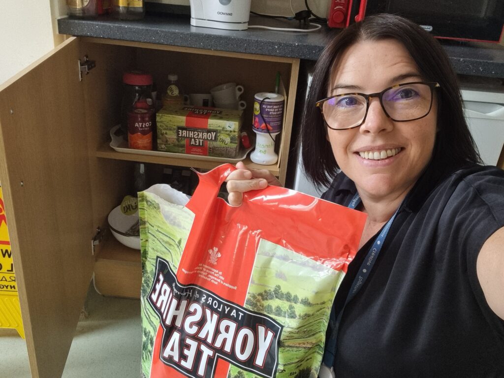Catherine, holding a big bag of Yorkshire Tea Bags next to an open kitchen cupboard.