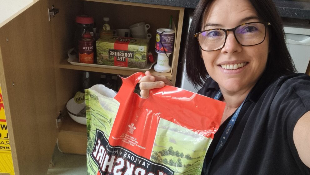 Catherine, holding a big bag of Yorkshire Tea Bags next to an open kitchen cupboard.